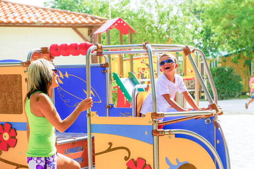 Niño riendo y mujer en área de juegos en el camping CAPFUN Huttes en Saint-Denis d'Oléron.
